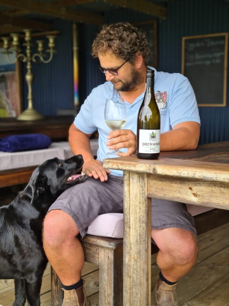 Wine maker Sollie Sauerman and his dog Margaret sitting at a table drinking Packwood wine